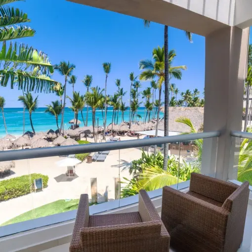 Suite balcony with wicker chairs overlooking the beach and palm trees at Royalton Punta Cana, Punta Cana