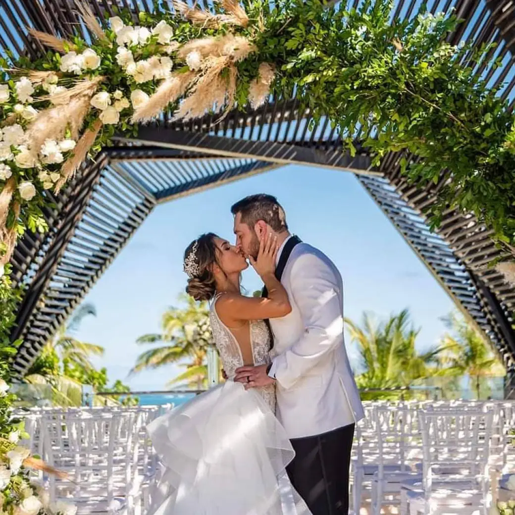 The couple's first kiss under a floral arch at Royalton Riviera Cancun