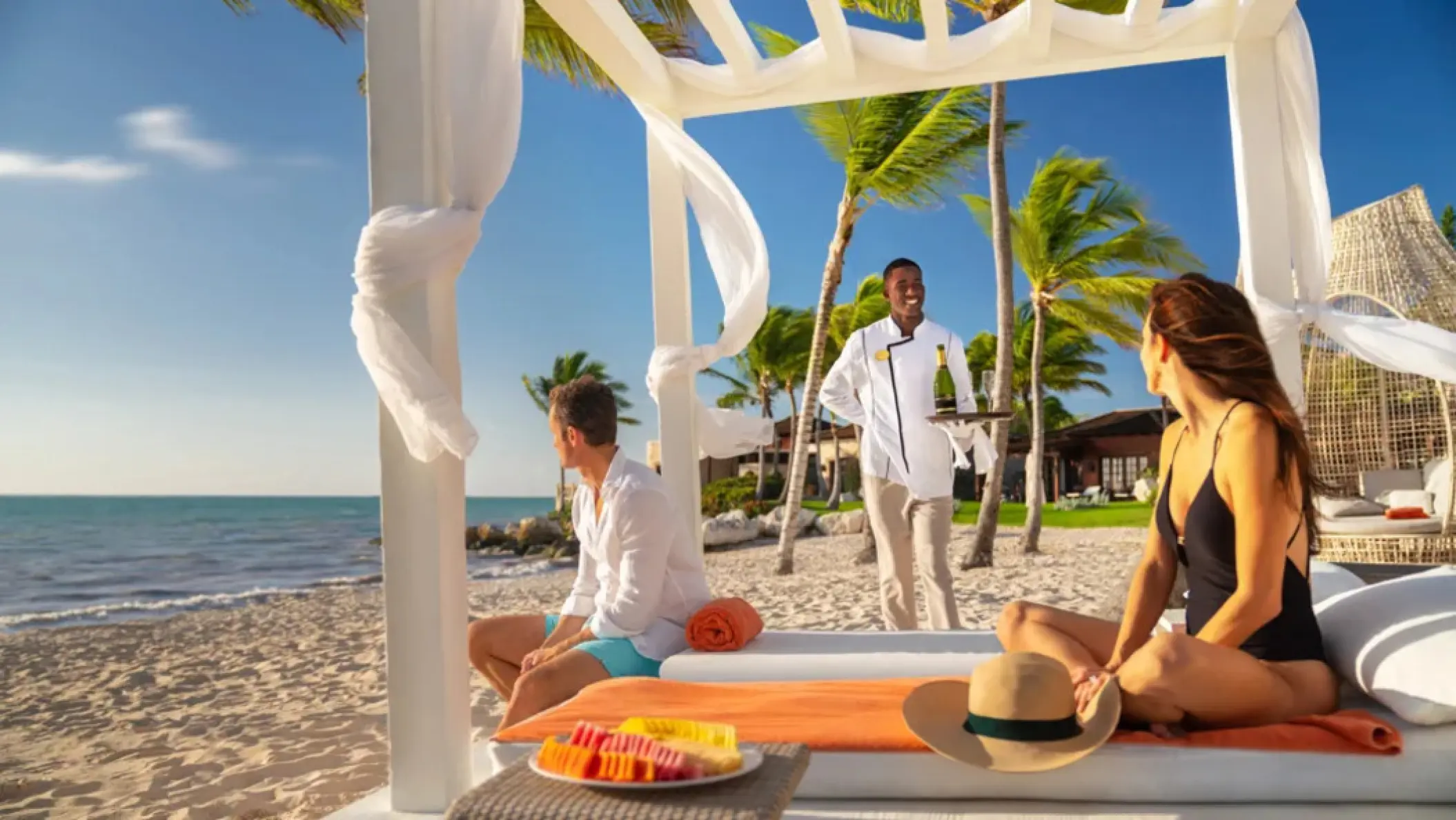 A server bringing champagne to a couple in a beach cabana at Sanctuary Cap Cana, Punta Cana