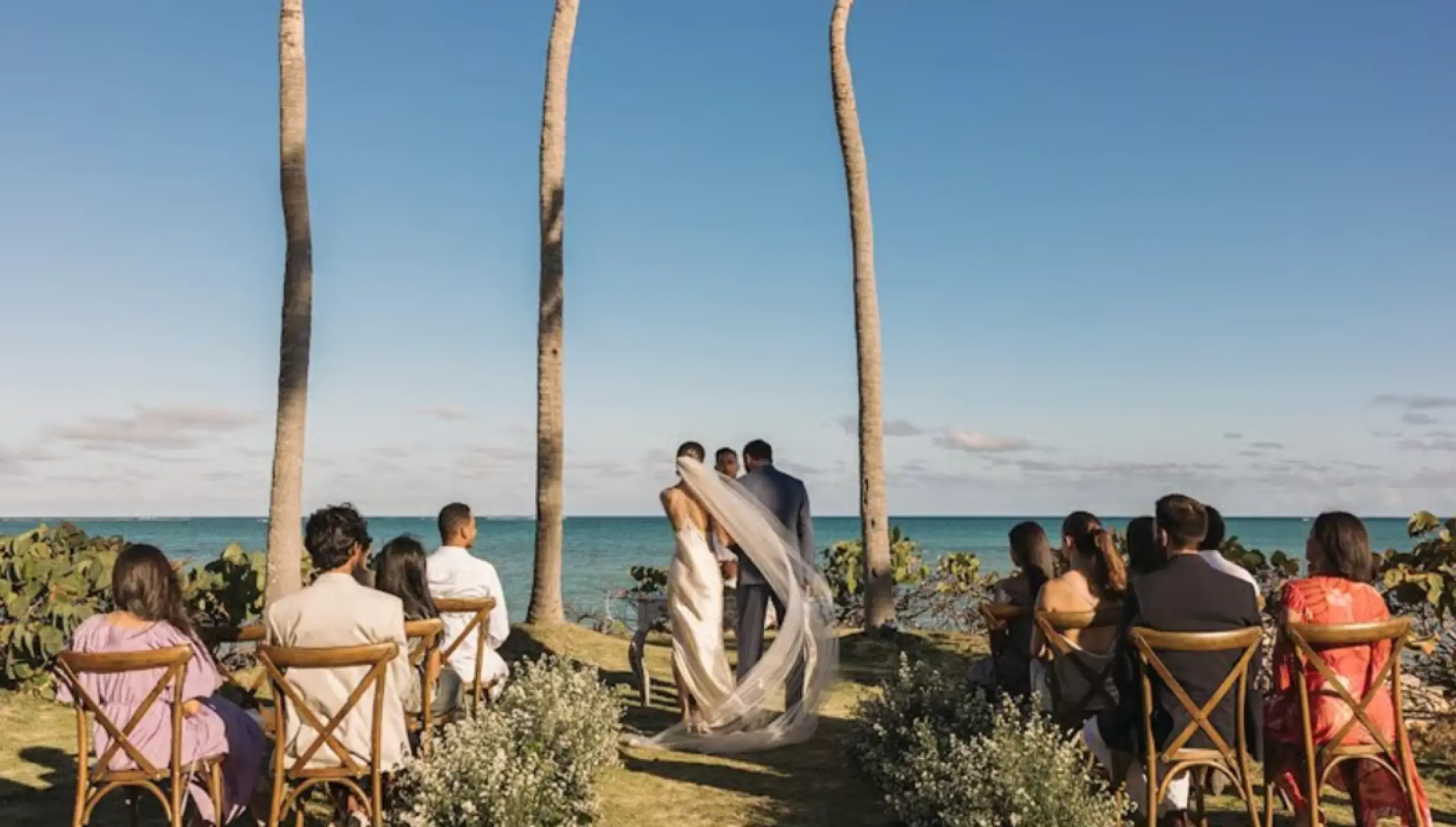 Wedding ceremony at Sanctuary Cap Cana, Punta Cana with ocean views and guests seated under palm trees