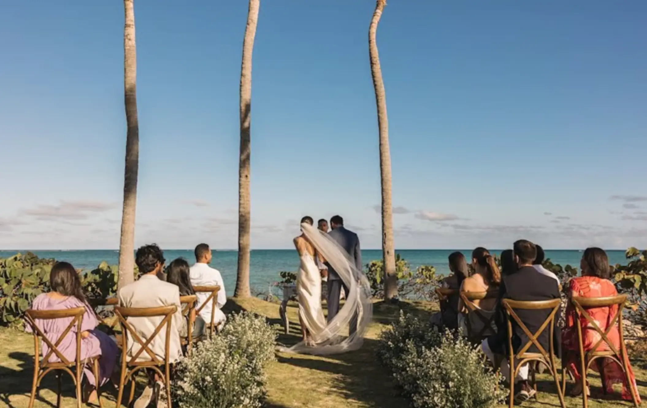 Wedding ceremony at Sanctuary Cap Cana, Punta Cana with ocean views and guests seated under palm trees