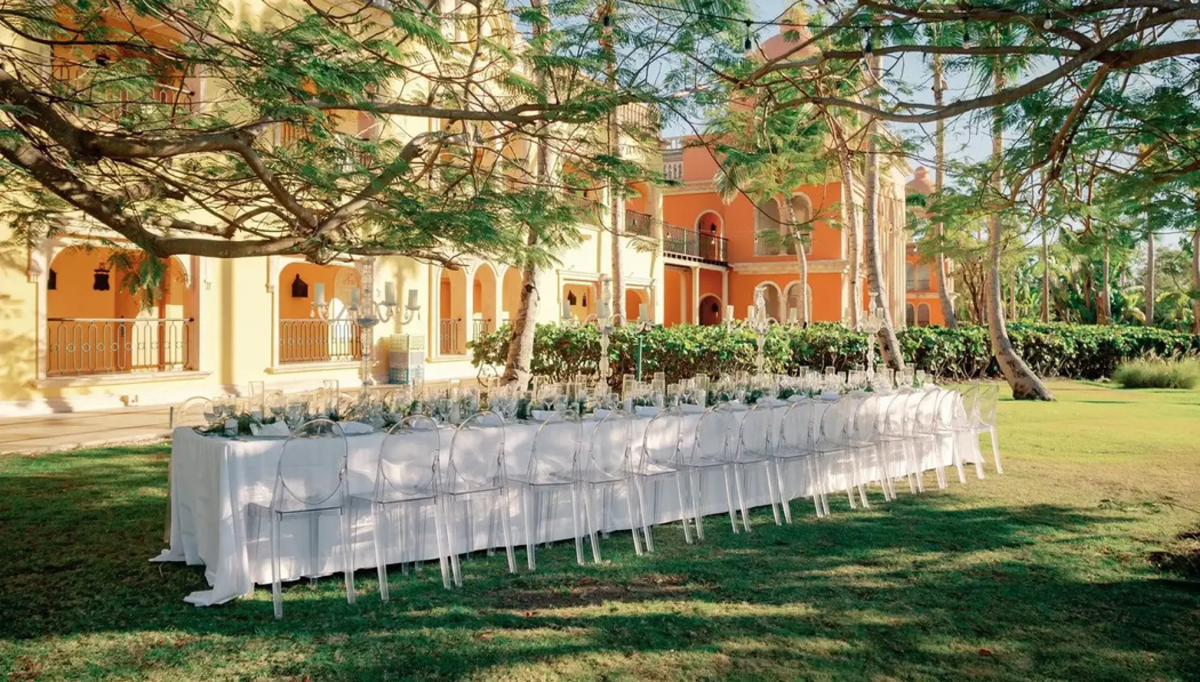 Garden wedding reception setup with long banquet table and clear chairs at Sanctuary Cap Cana, Punta Cana