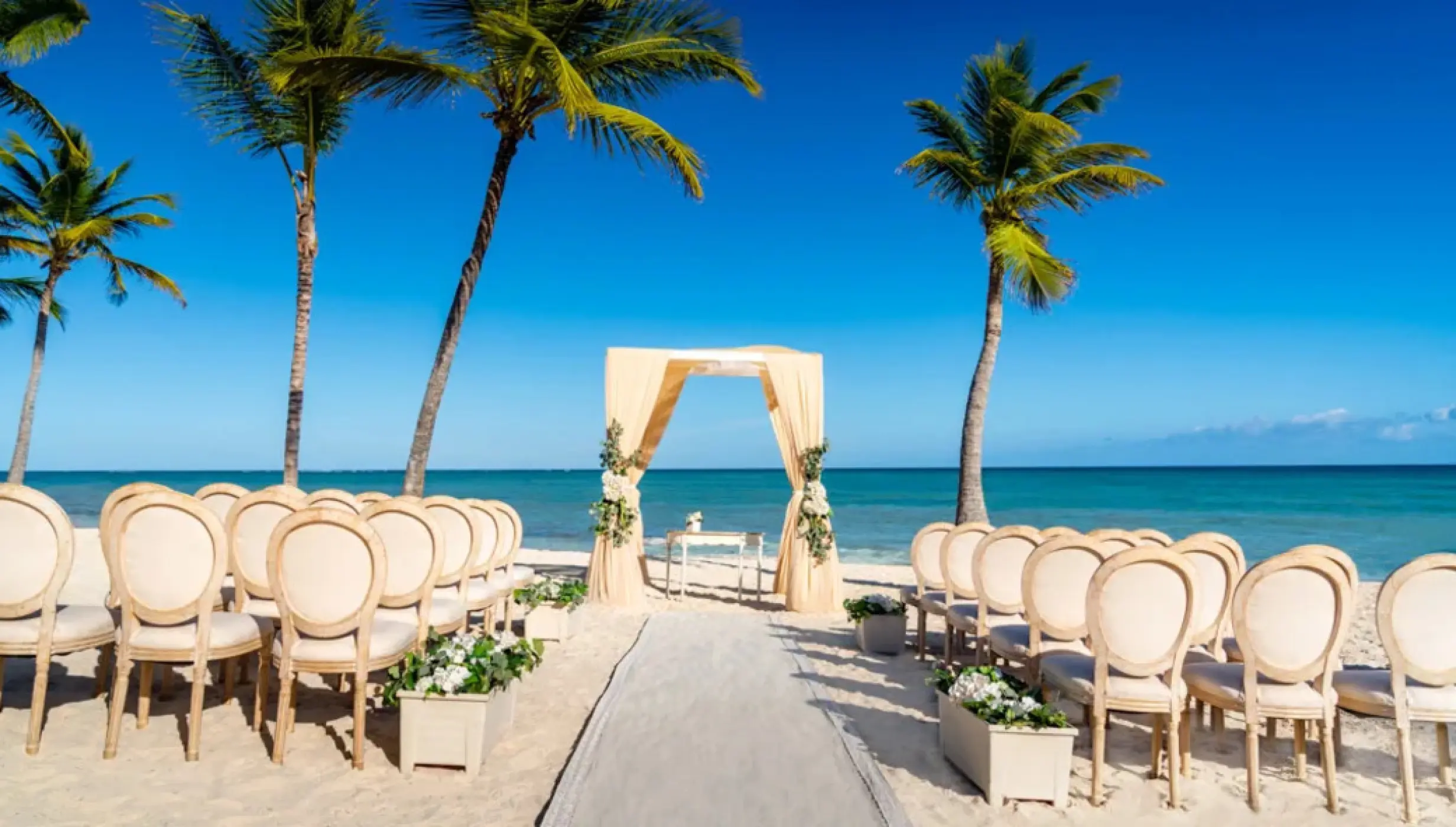 Beachfront wedding ceremony with draped arch and palm trees at Sanctuary Cap Cana, Punta Cana