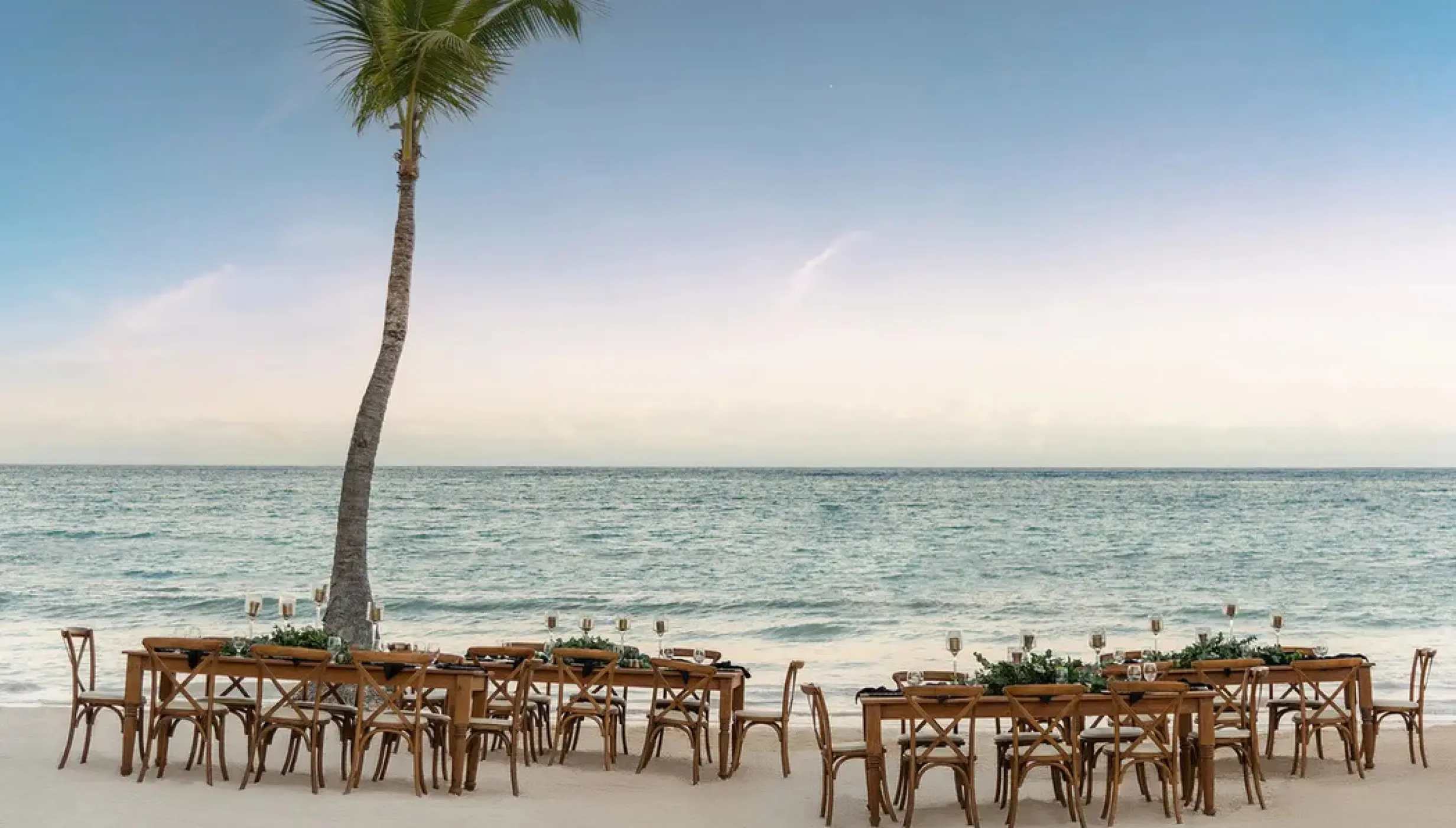 Beachfront wedding reception setup with wooden tables and chairs at Sanctuary Cap Cana, Punta Cana