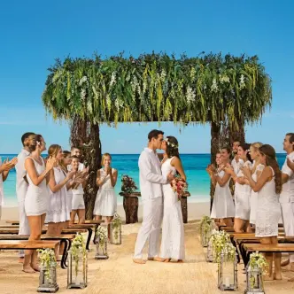 Bride and groom kissing under a greenery arch during a beach ceremony at Secrets Akumal, Riviera Maya