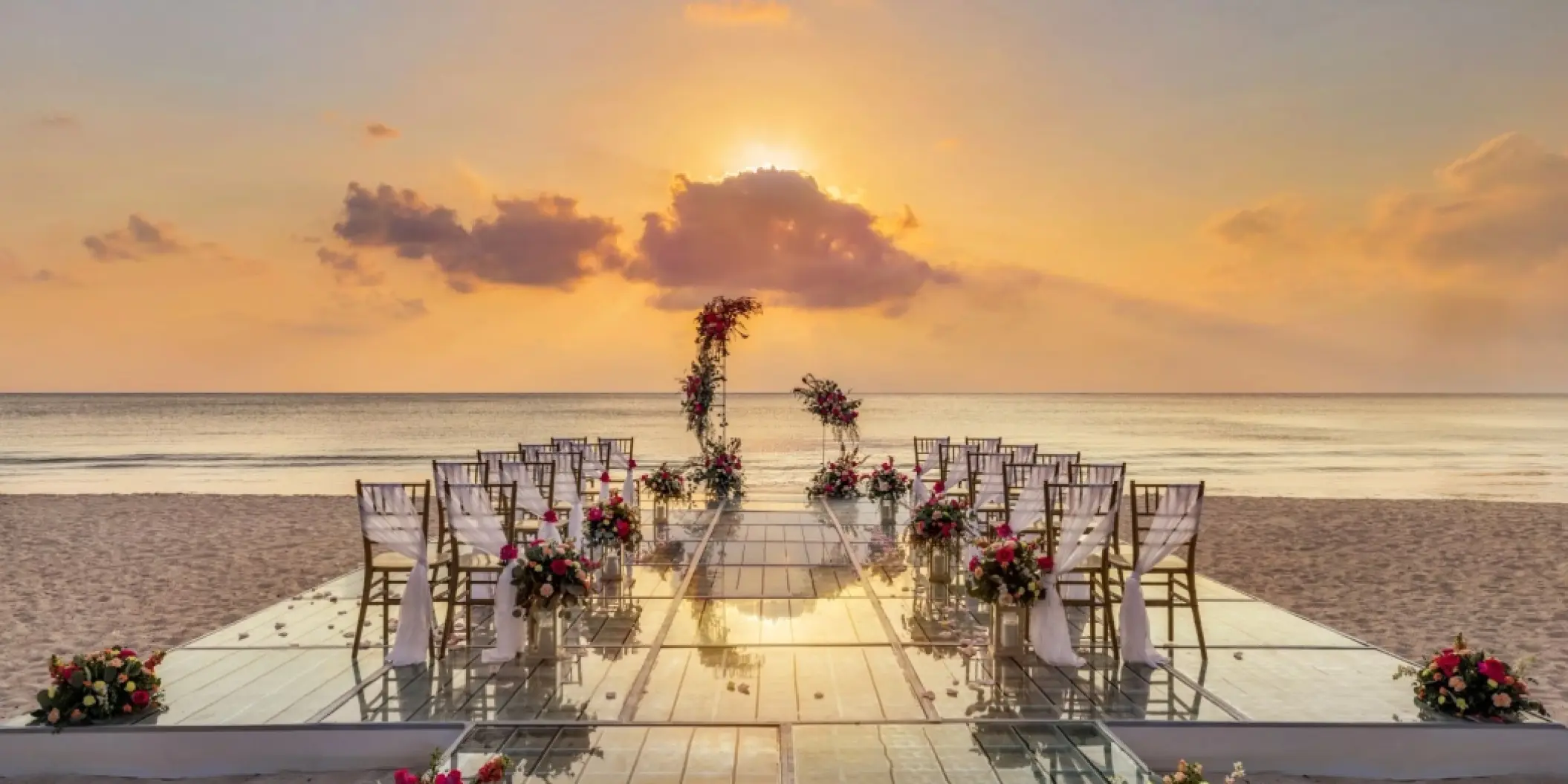 Beachfront wedding ceremony setup on a glass platform at sunset at Secrets Aura Cozumel
