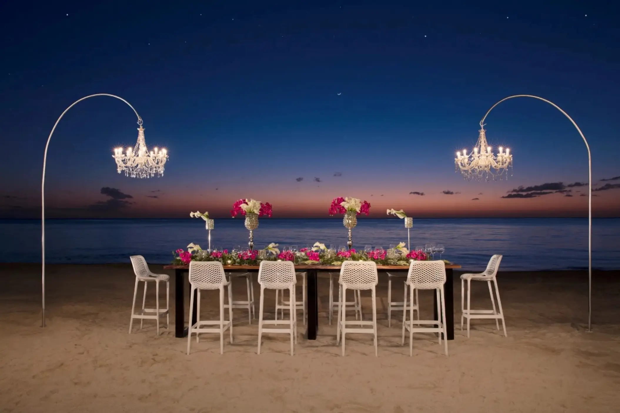 Beachfront wedding reception setup with chandeliers and pink flowers at Secrets Aura Cozumel
