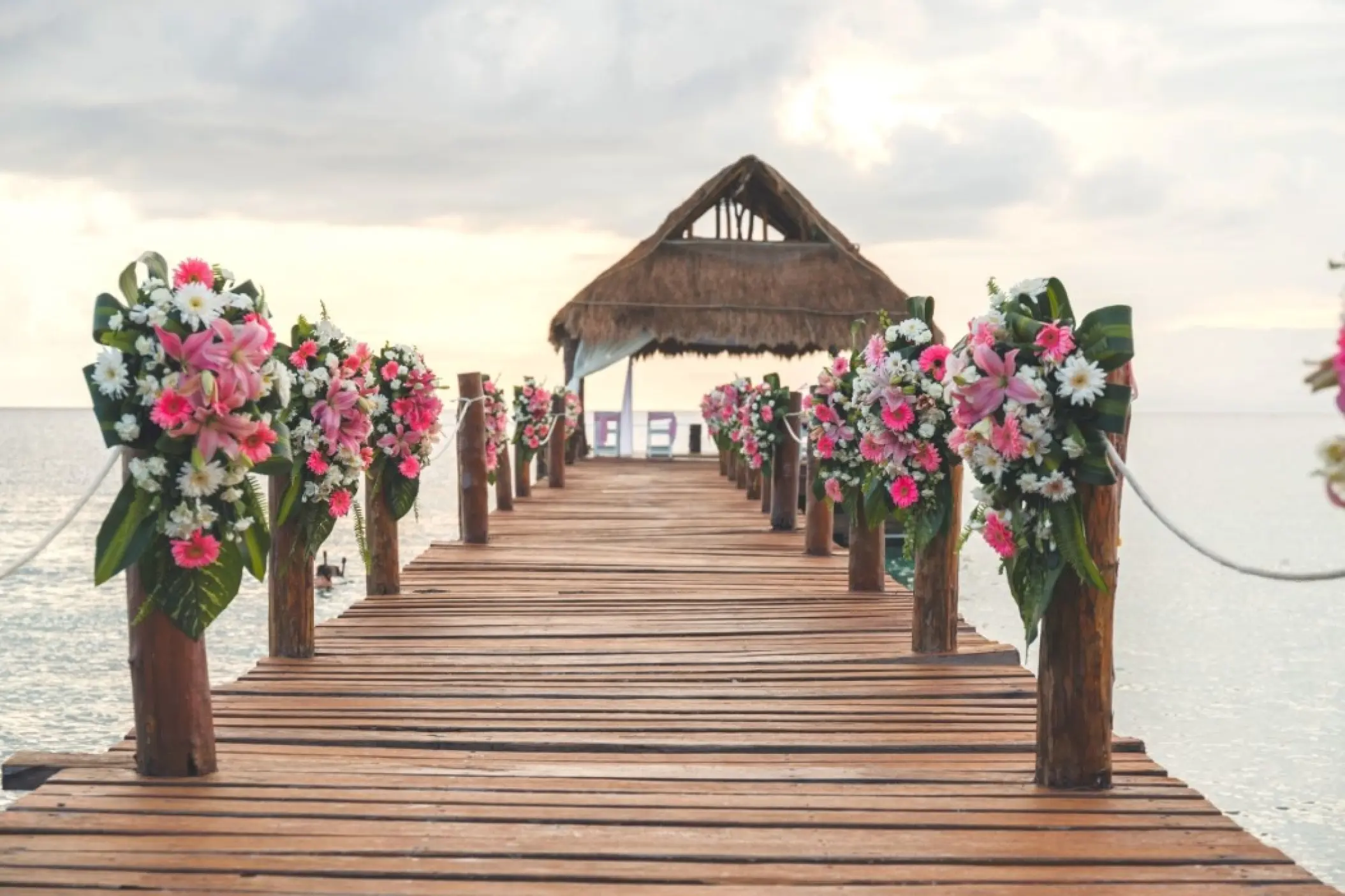 Pier wedding ceremony setup with pink flowers and a thatched palapa at Secrets Aura Cozumel