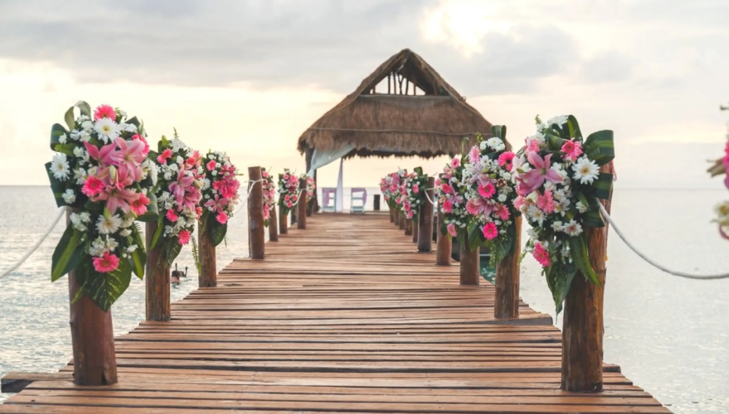 Pier wedding ceremony setup with pink flowers and a thatched palapa at Secrets Aura Cozumel