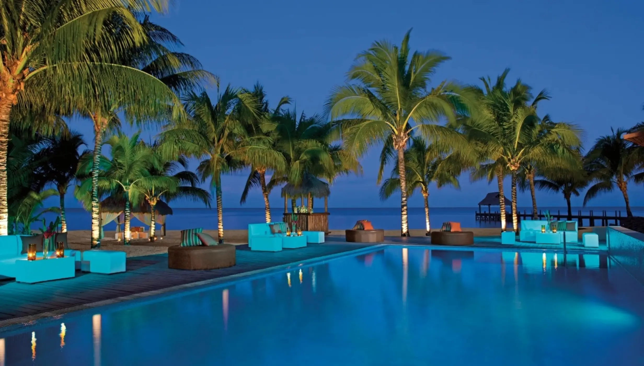 Poolside lounge area at night overlooking the ocean at Secrets Aura Cozumel
