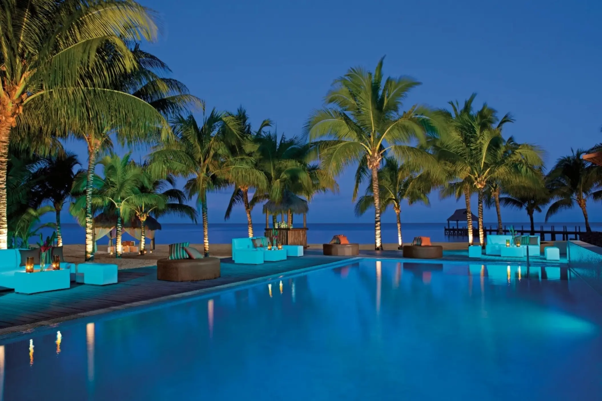 Poolside lounge area at night overlooking the ocean at Secrets Aura Cozumel