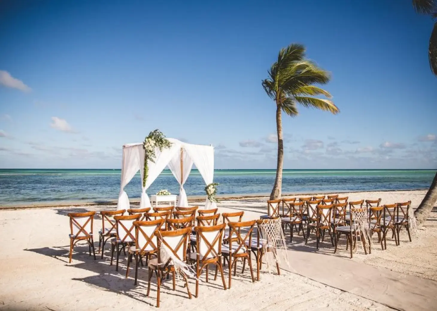 Beachfront wedding ceremony with white canopy and wooden chairs at Secrets Cap Cana, Punta Cana
