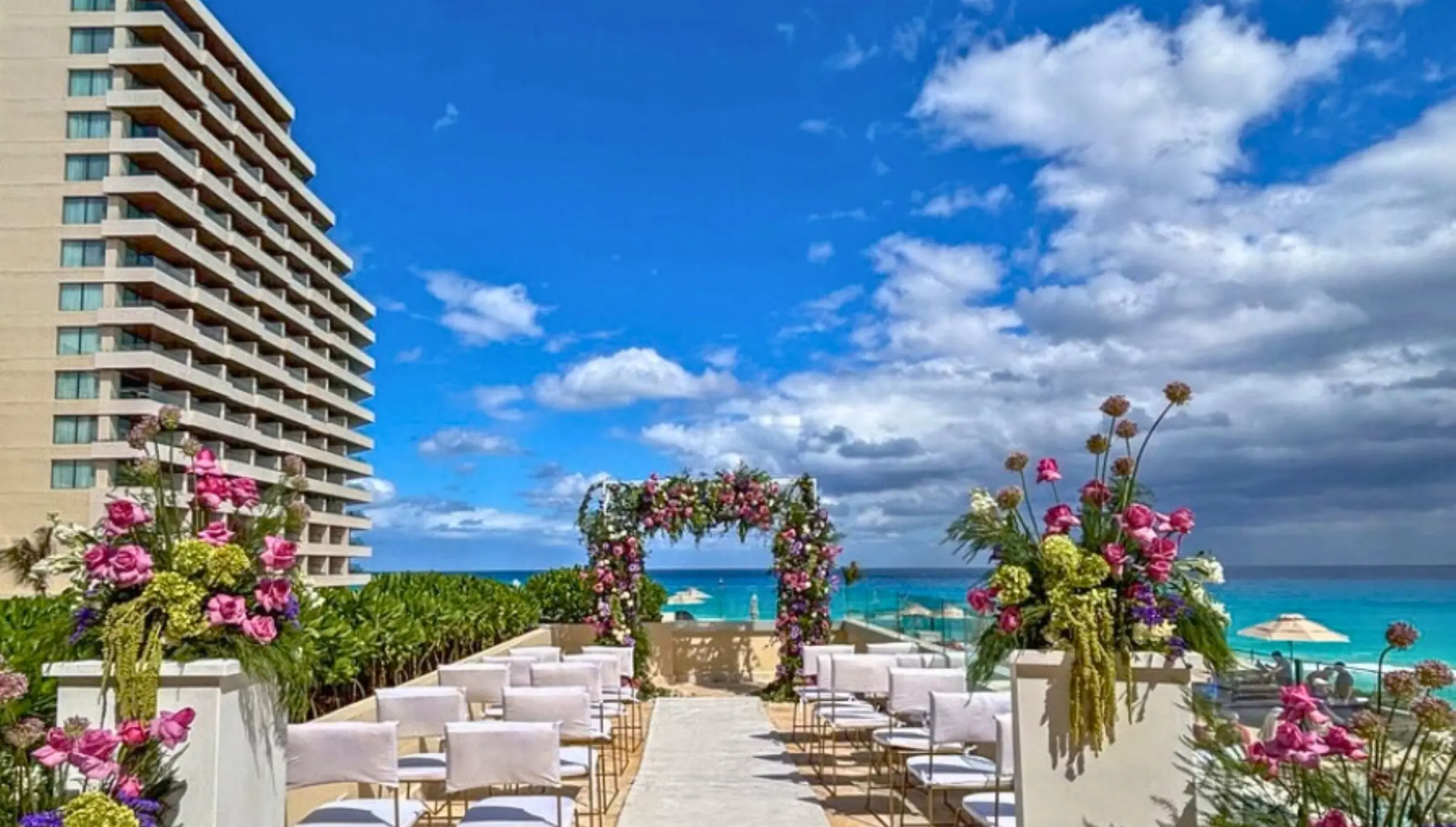 Pool deck wedding ceremony with floral arch and white chairs at Secrets Mirabel, Cancun