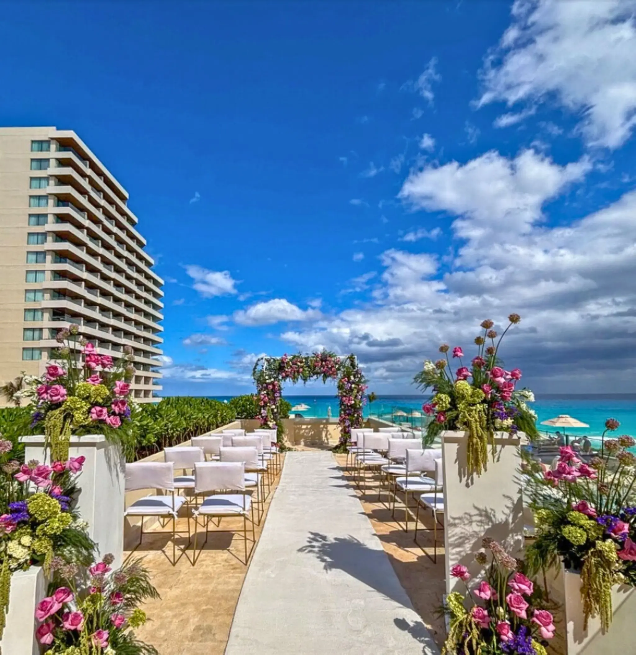 Pool deck wedding ceremony with floral arch and white chairs at Secrets Mirabel, Cancun