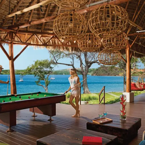 Couple playing pool at an open-air bar at Secrets Papagayo overlooking the water, Papagayo