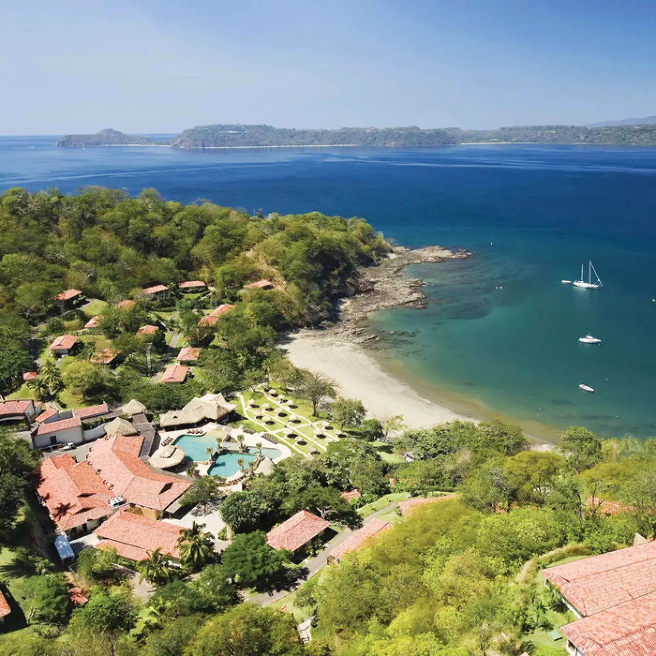 Aerial view of Secrets Papagayo buildings and pool nestled in lush greenery by the beach, Papagayo