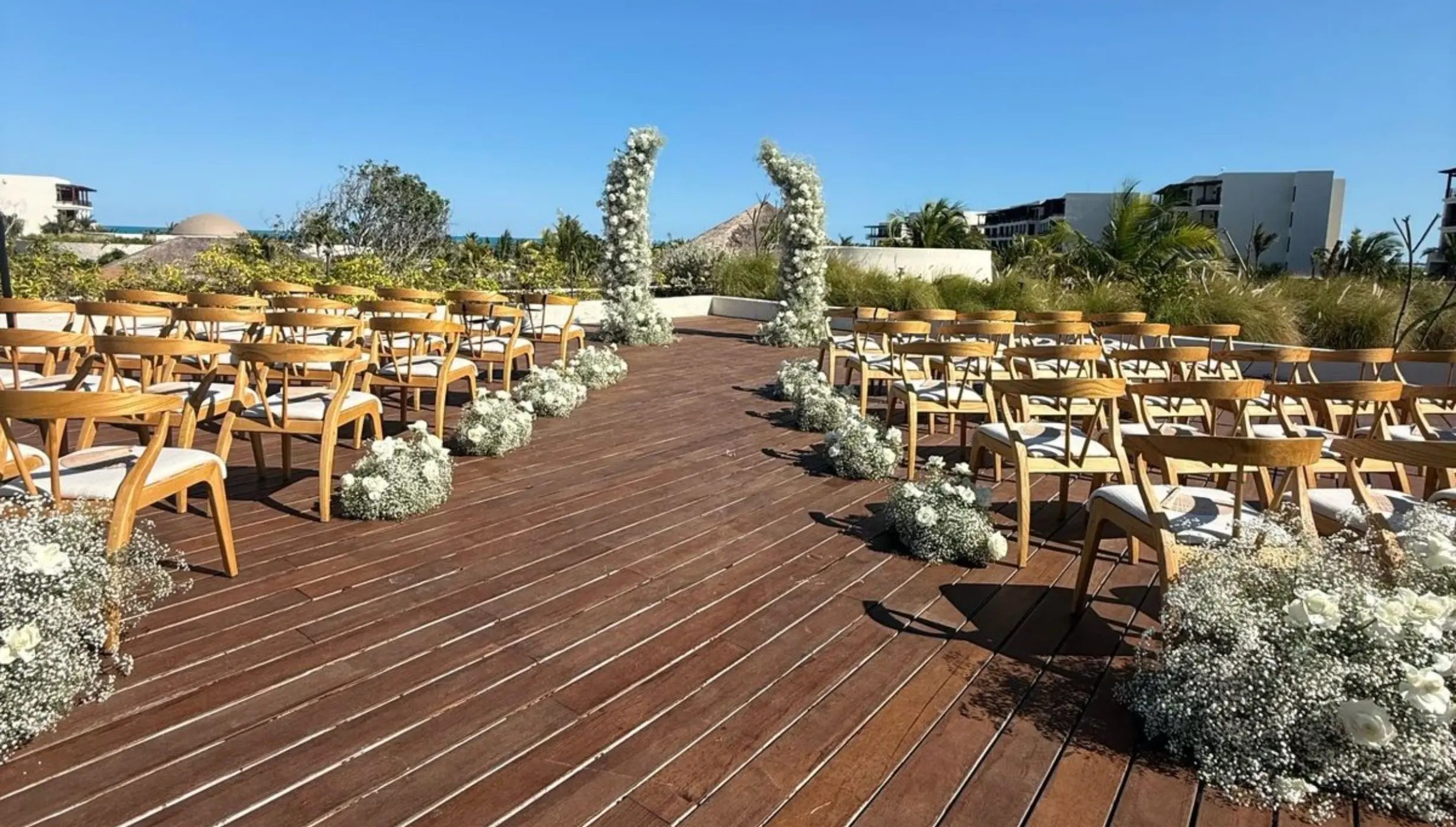 Rooftop wedding ceremony setup with white floral arch and wooden chairs at Secrets Playa Blanca, Cancun
