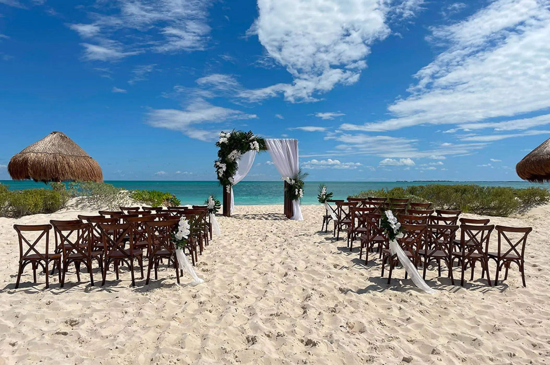 Beachfront wedding ceremony setup with wooden cross-back chairs at Secrets Playa Blanca, Cancun