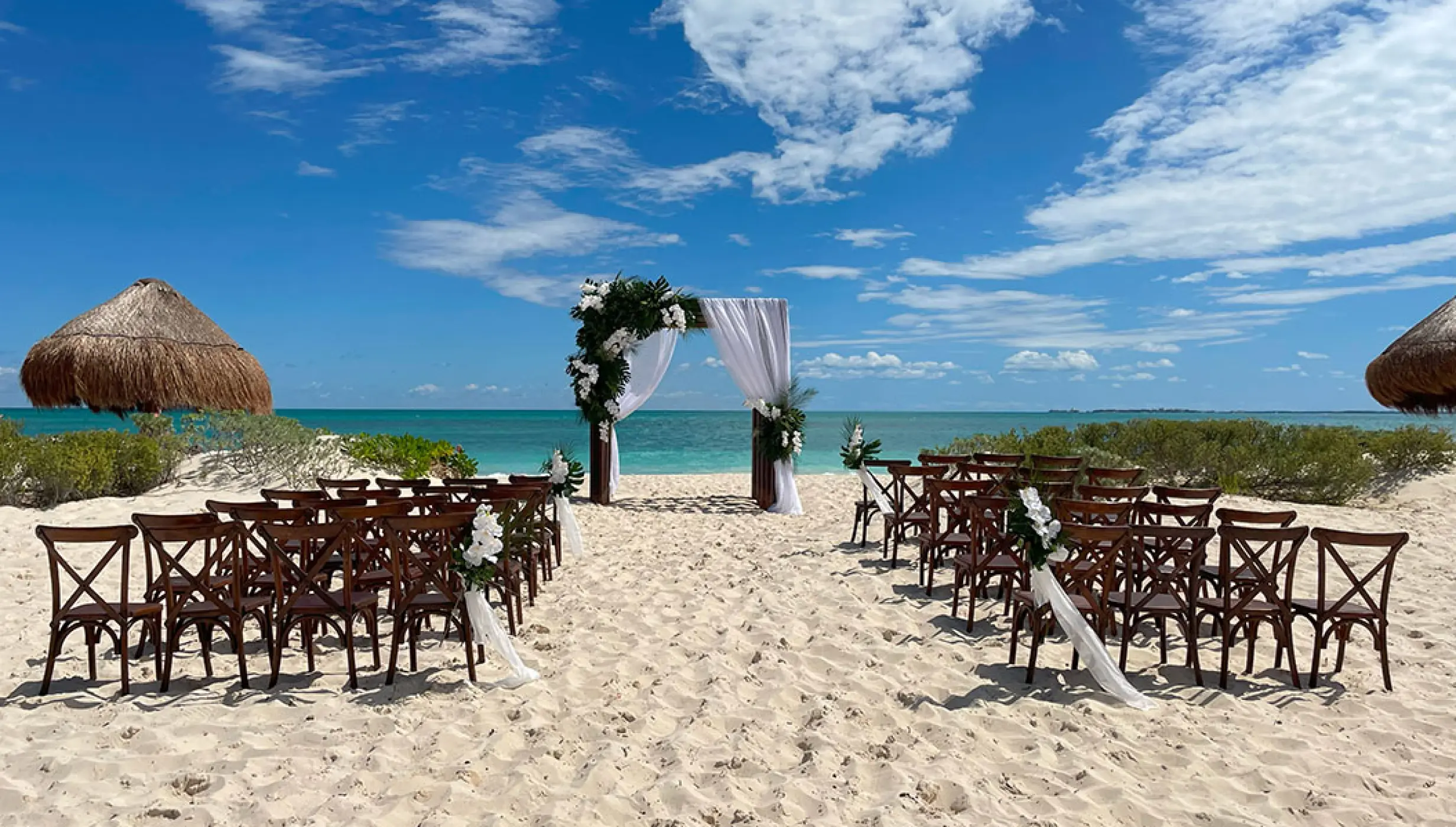 Beachfront wedding ceremony setup with wooden cross-back chairs at Secrets Playa Blanca, Cancun