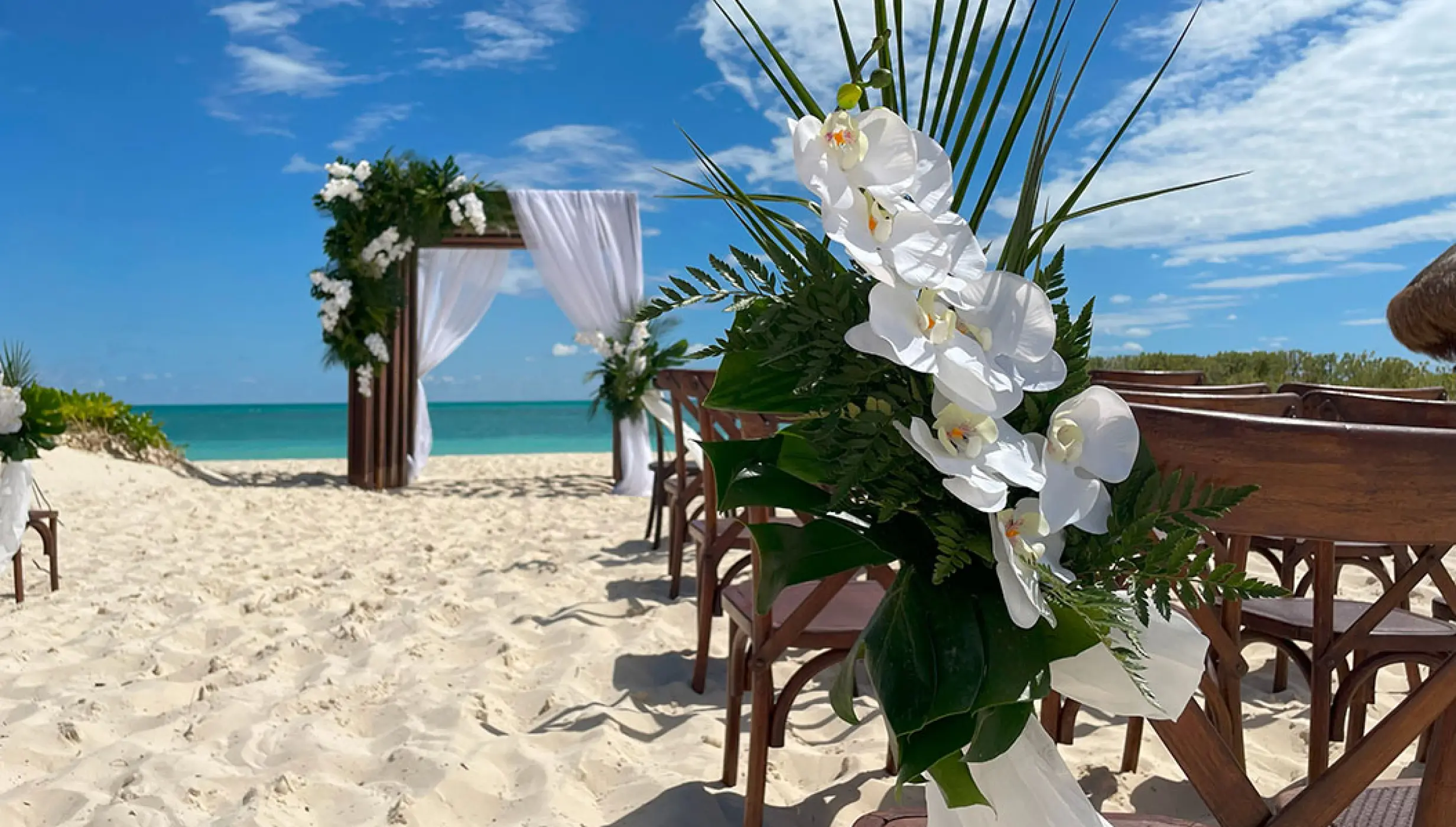 Beach wedding ceremony with white orchids and a wooden arch at Secrets Playa Blanca, Cancun