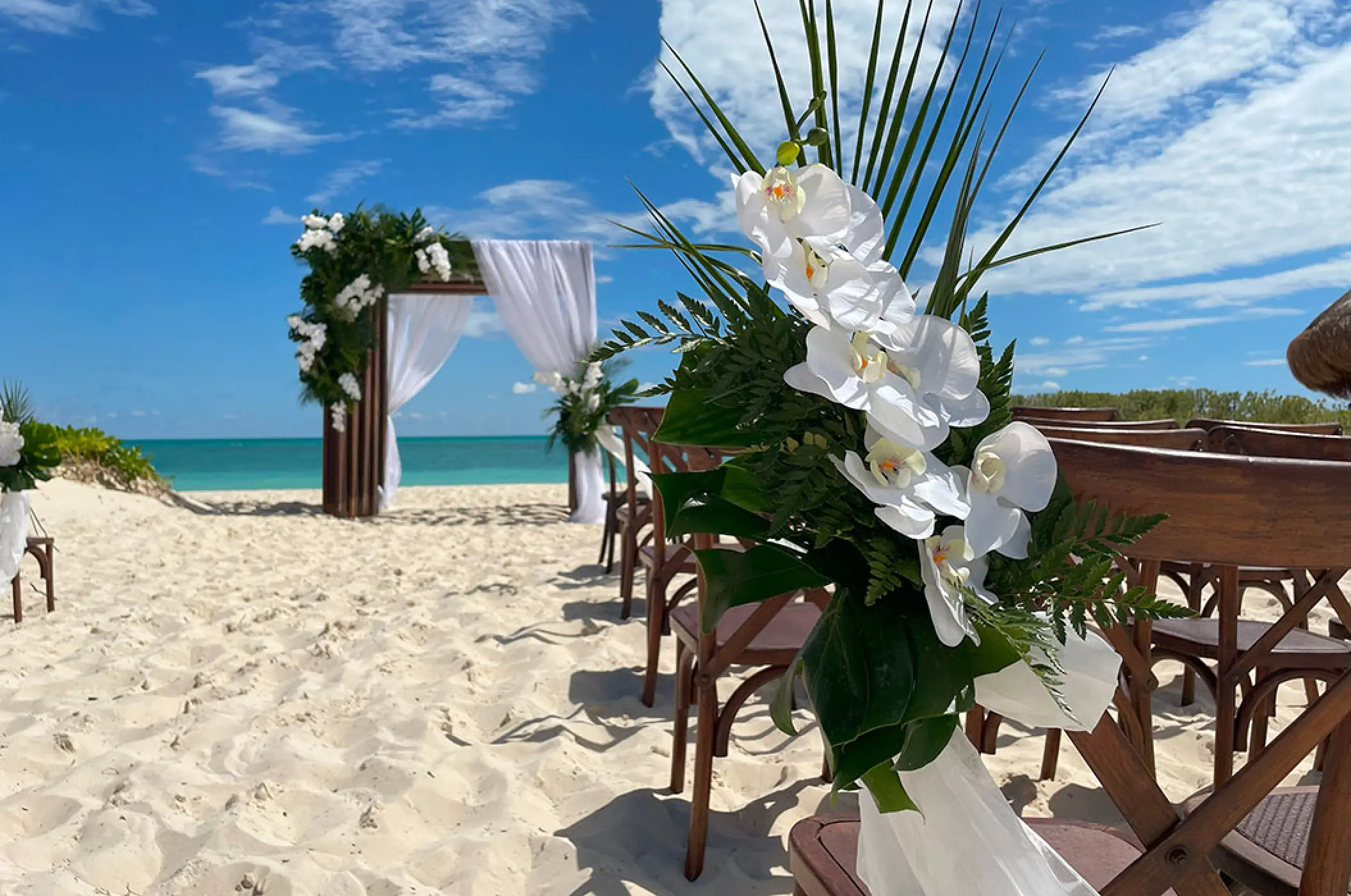 Beach wedding ceremony with white orchids and a wooden arch at Secrets Playa Blanca, Cancun