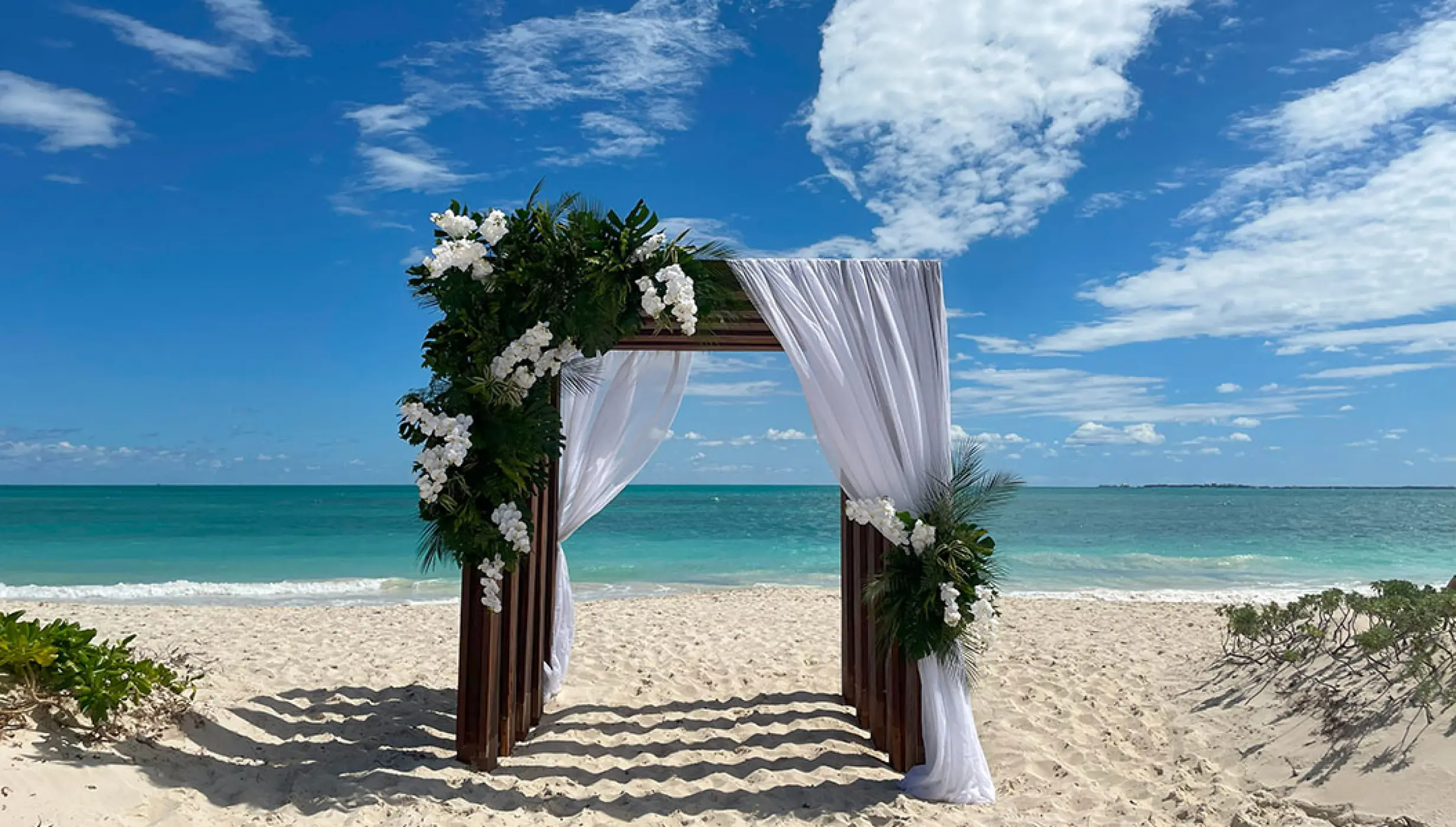 Beachfront wedding ceremony arch with white flowers and drapes at Secrets Playa Blanca, Cancun
