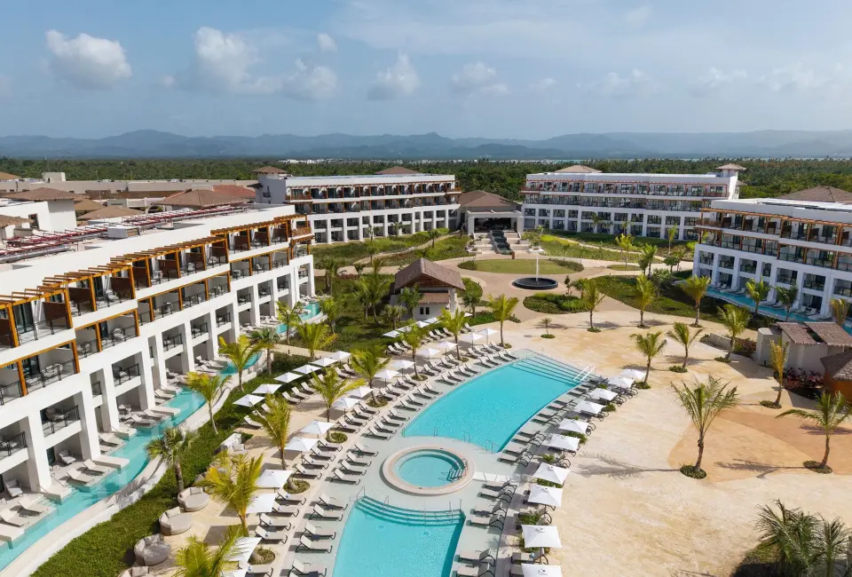 An aerial view of the Secrets Playa Esmeralda resort with a large pool, lounge chairs, and buildings.