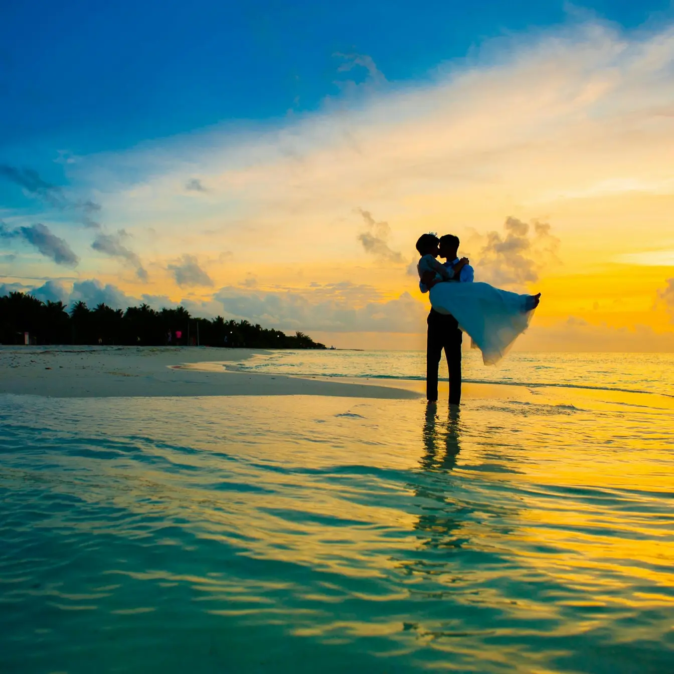 Groom carrying his bride in the ocean during a sunset wedding at Secrets Playa Esmeralda, Miches