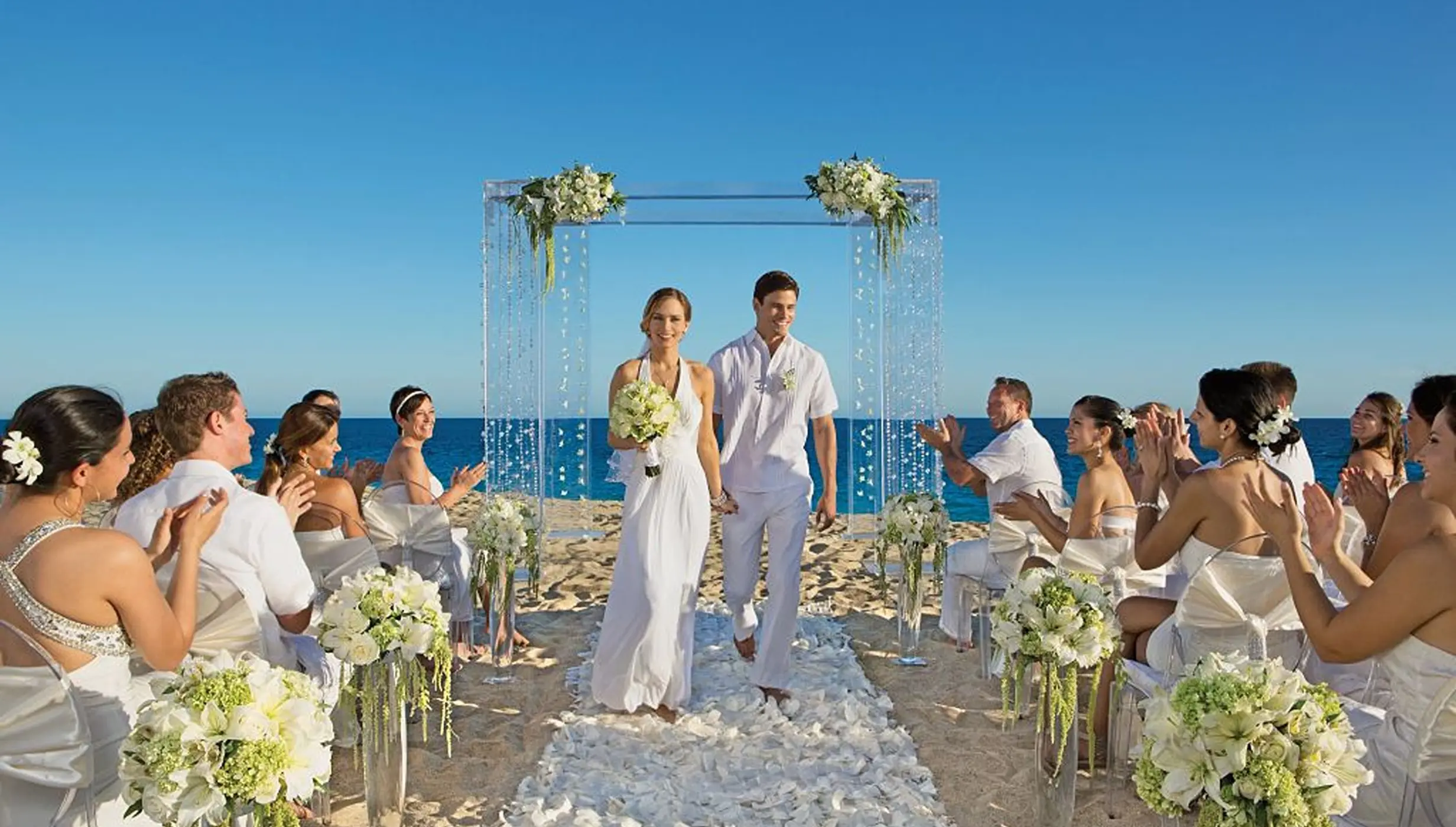 Newlyweds walking down a petal-covered aisle during a beach ceremony at Secrets Playa Esmeralda, Miches