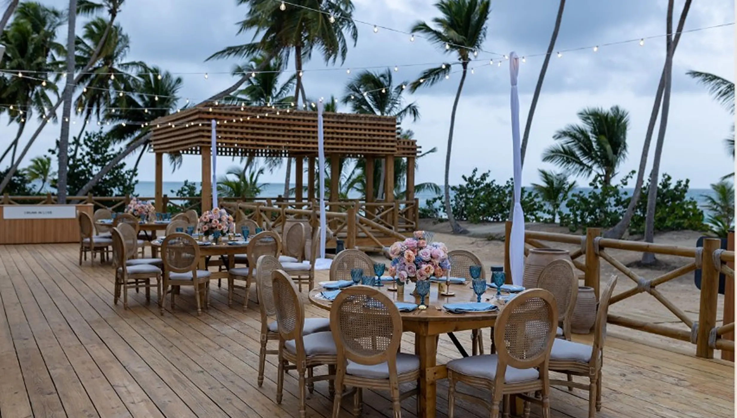 Outdoor wedding reception on a wooden deck with palm trees at Secrets Playa Esmeralda, Miches