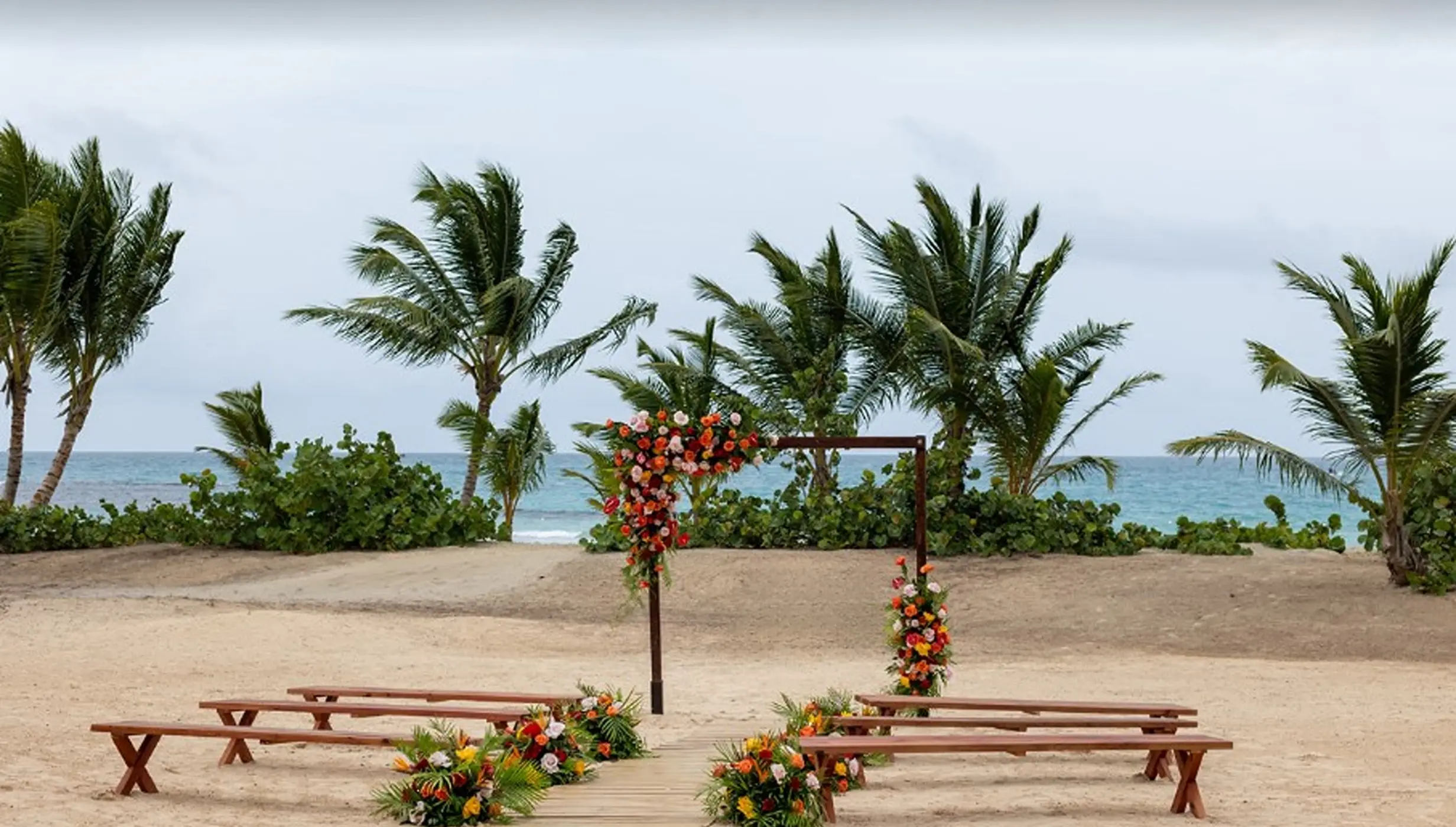 Beachfront wedding ceremony with wooden benches and floral arch at Secrets Playa Esmeralda, Miches