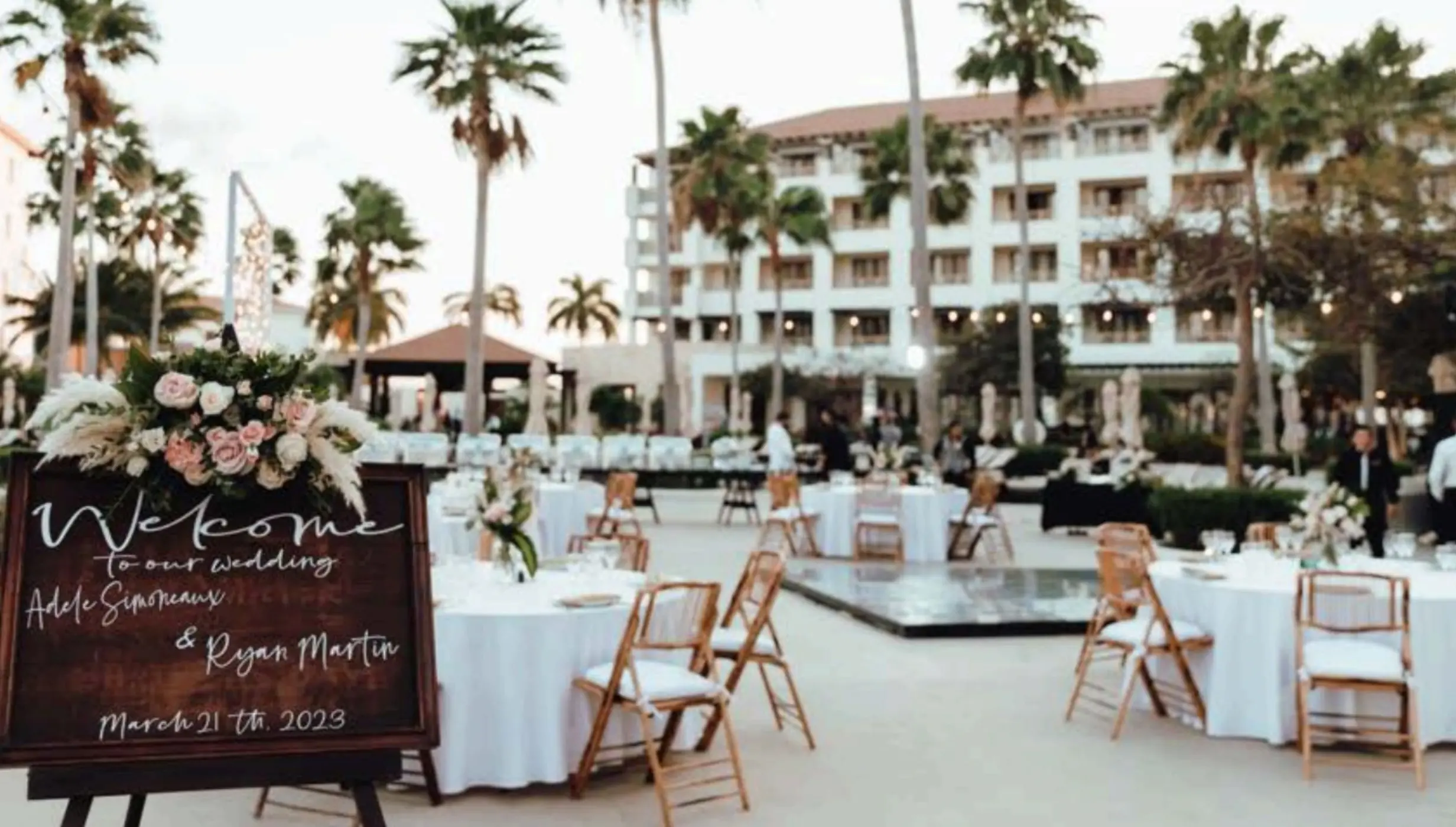 Outdoor wedding reception setup at Secrets Playa Mujeres, Cancun with a wooden welcome sign and palm trees
