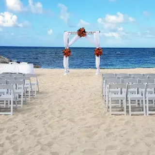 Beachfront wedding ceremony with white chairs and floral arch at Secrets St James, Montego Bay
