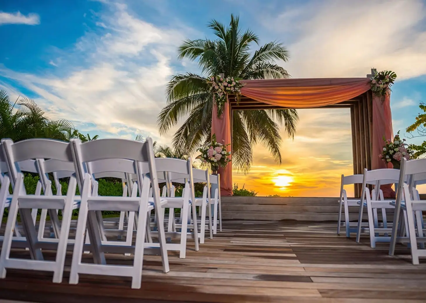 Sunset beach wedding ceremony with floral gazebo and white chairs at Secrets St James, Montego Bay