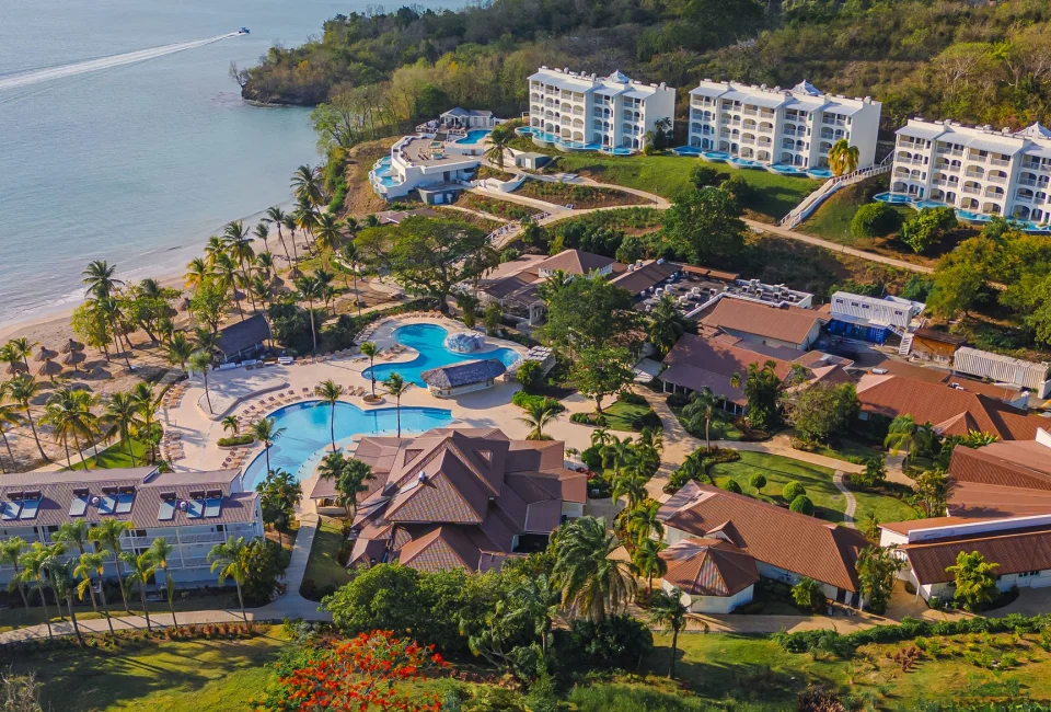 An aerial view of Secrets St. Lucia resort, showcasing pools, buildings, and a beach along the coast.