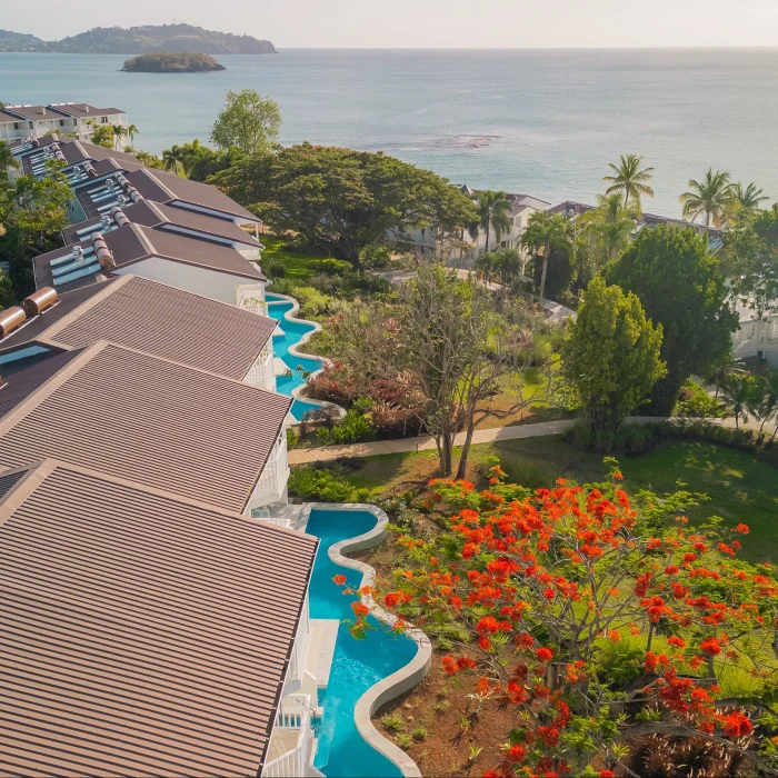 An aerial view of a resort with swim-up suites and lush greenery leading to the ocean.