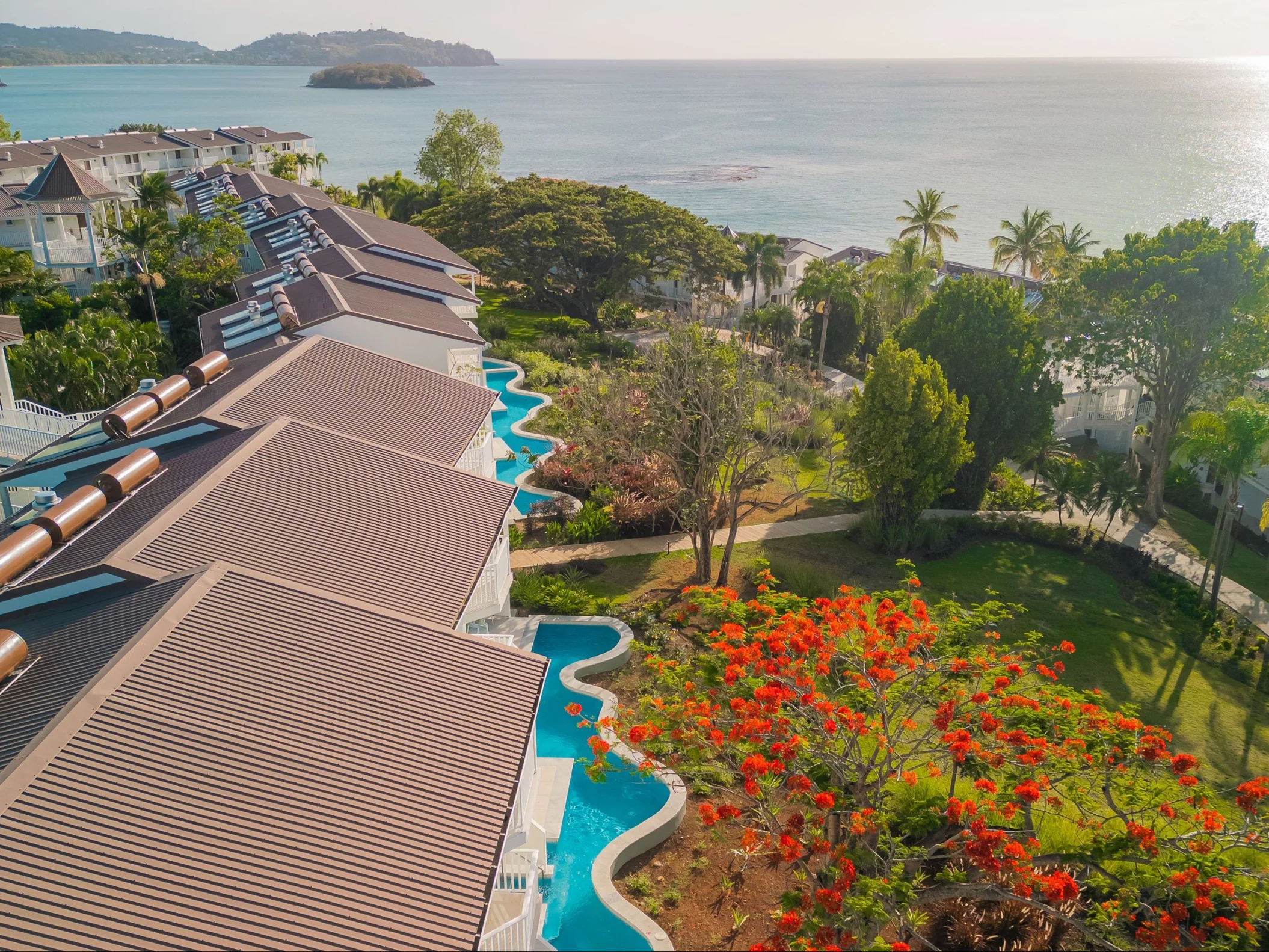 An aerial view of a resort with swim-up suites and lush greenery leading to the ocean.