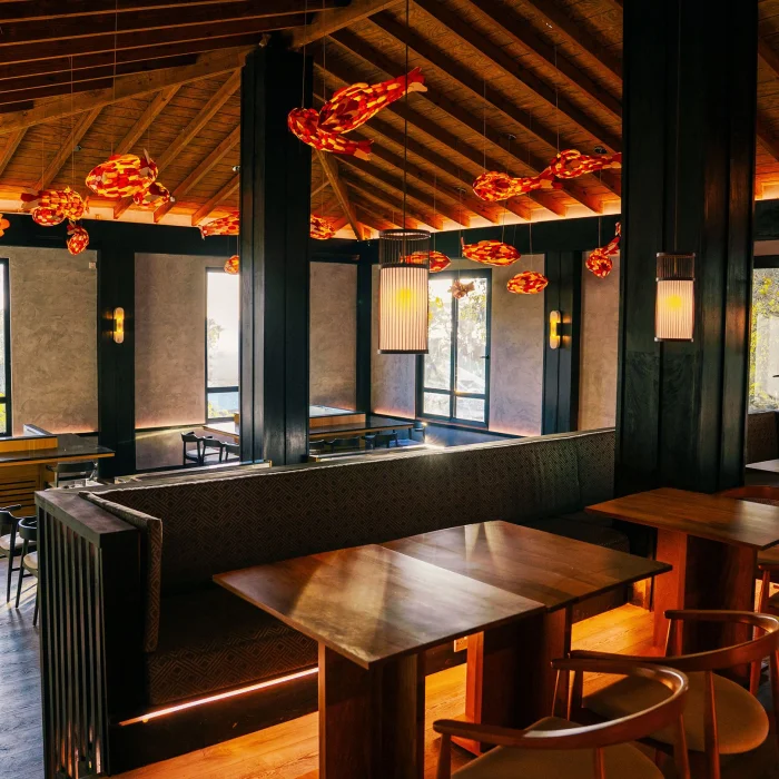 An inviting restaurant with warm lighting, wooden tables, and unique fish-shaped hanging decorations.