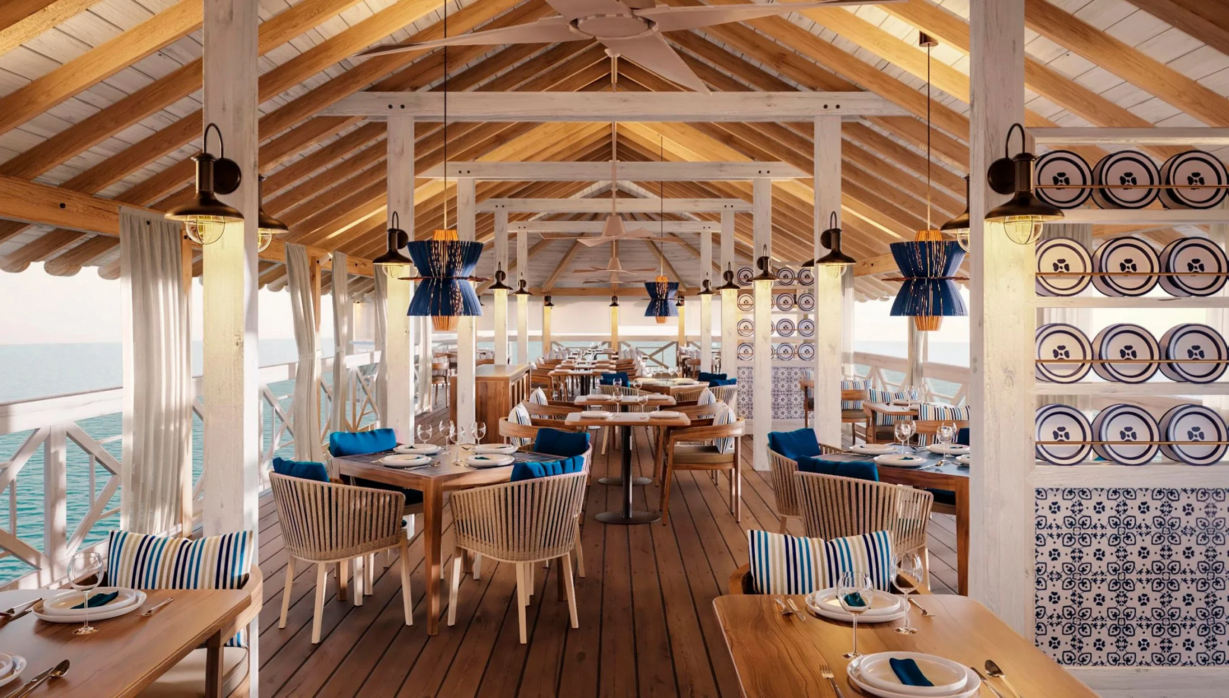 A spacious overwater restaurant with high ceilings, wooden beams, and blue and white themed decor.