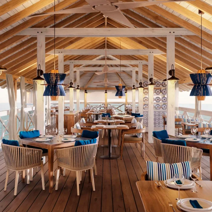 A spacious overwater restaurant with high ceilings, wooden beams, and blue and white themed decor.