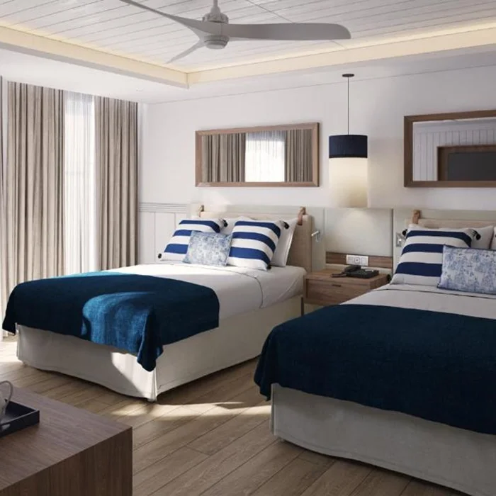 A well-lit hotel suite featuring two beds with blue and white striped bedding, and a sitting area.