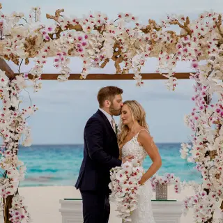 The couple sharing a forehead kiss under a floral arch at Secrets The Vine, Cancun