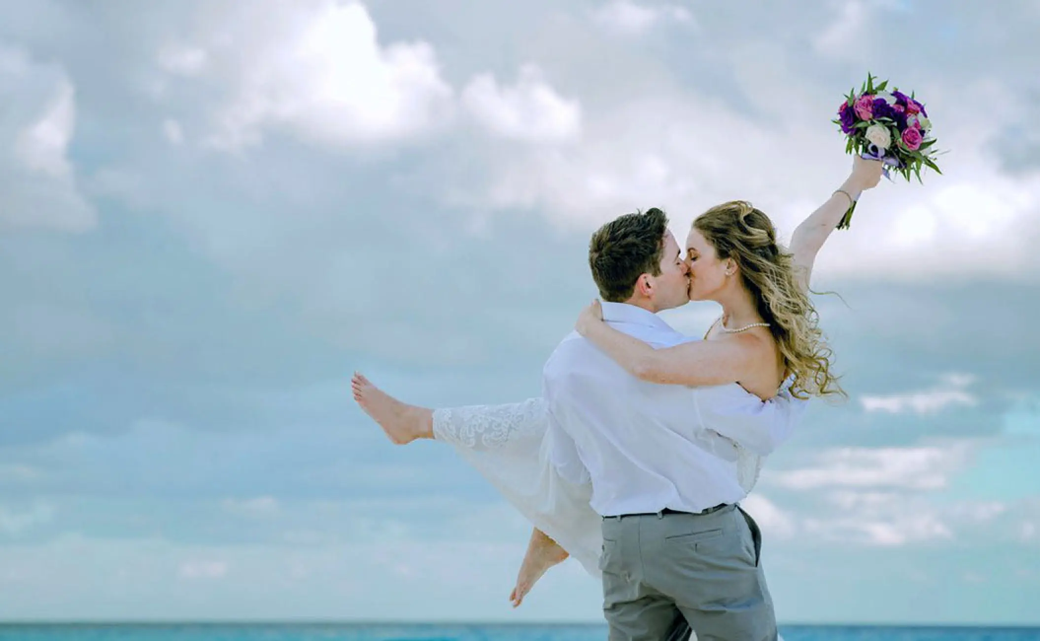 Groom carrying and kissing the bride during a beach wedding at Secrets The Vine, Cancun