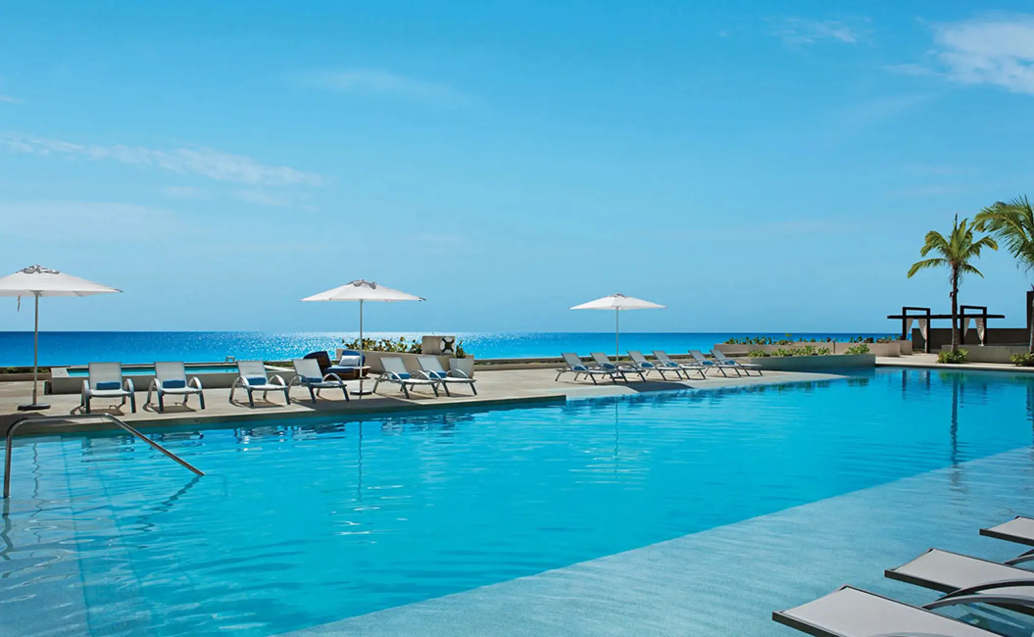 Secrets The Vine Cancun outdoor swimming pool with lounge chairs and umbrellas overlooking the ocean