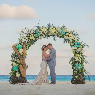 Bride and groom under a floral arch during a beach ceremony at Secrets The Vine, Cancun
