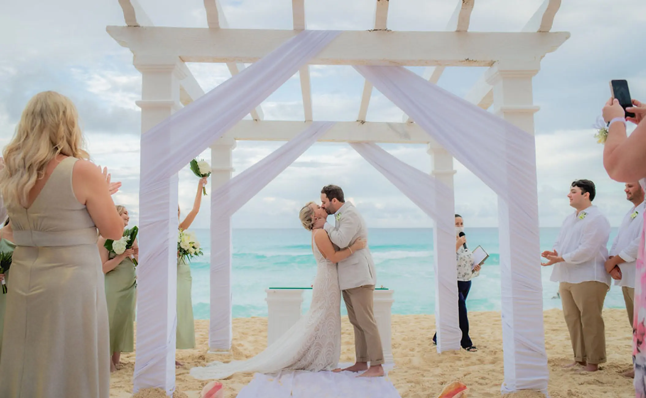 The couple kissing under a white pergola at a beach ceremony, Secrets The Vine Cancun