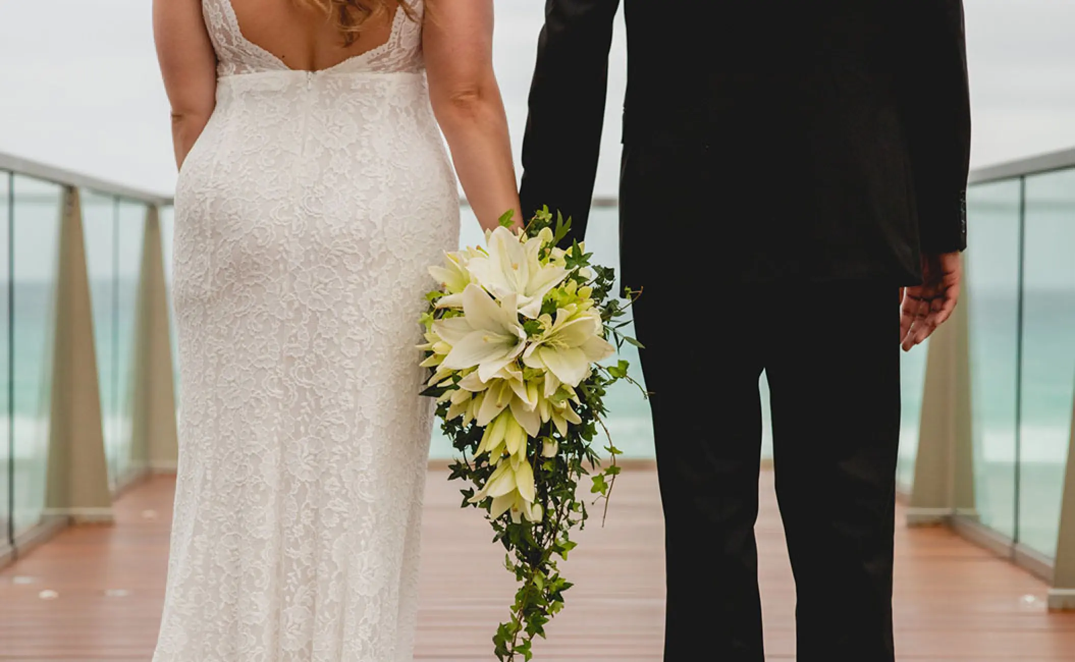 Bride and groom holding hands with a cascading lily bouquet at Secrets The Vine, Cancun