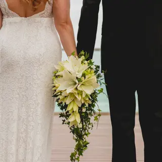 Bride and groom holding hands with a cascading lily bouquet at Secrets The Vine, Cancun