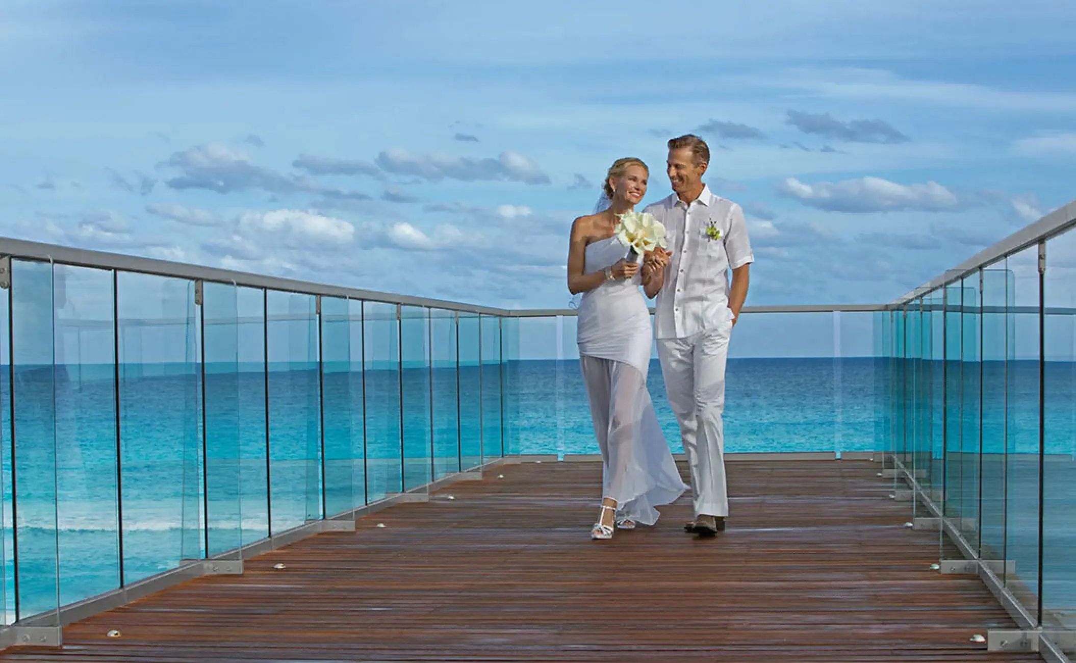 The bride and groom walking on a terrace overlooking the turquoise ocean at Secrets The Vine, Cancun