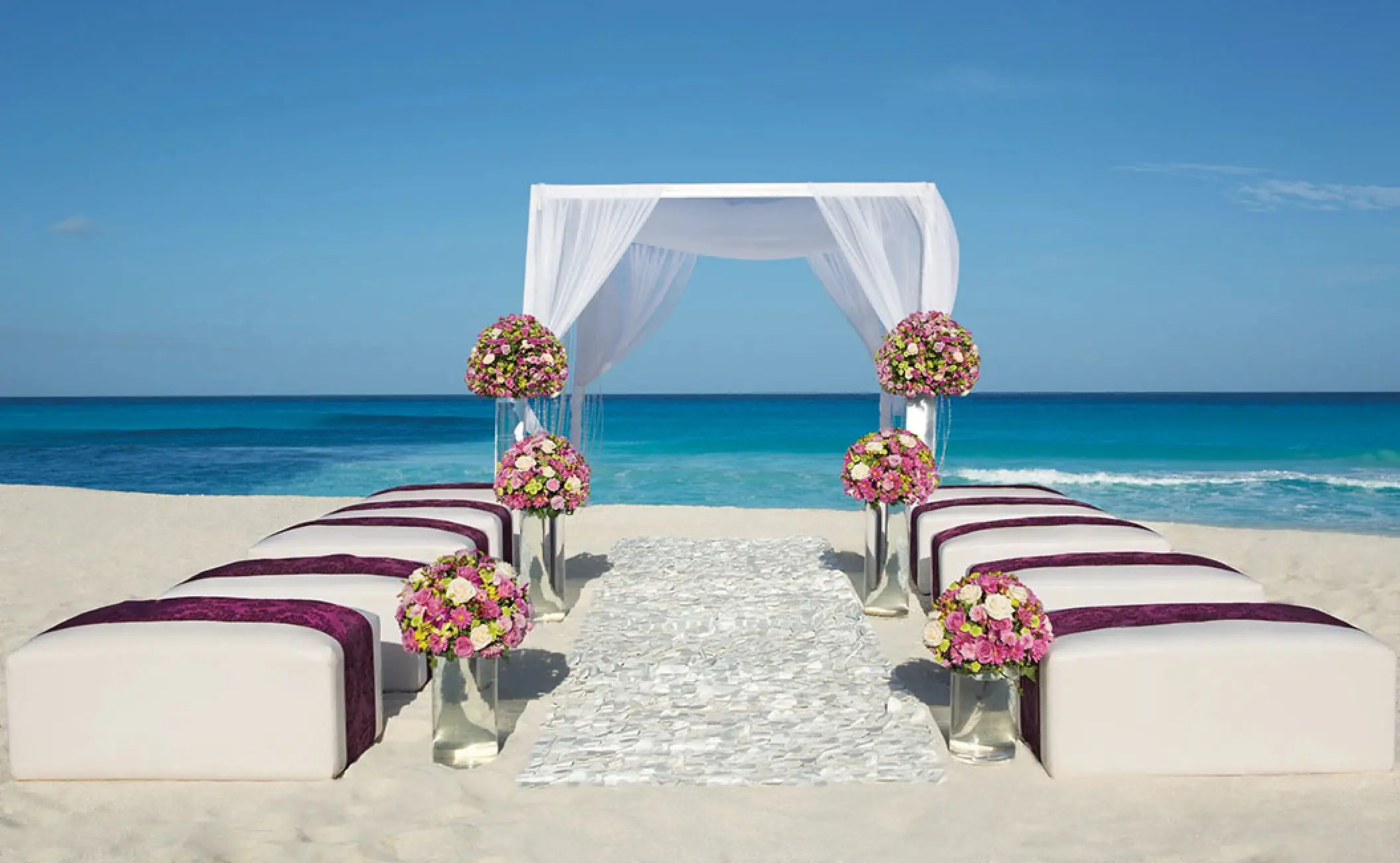 Beachfront wedding ceremony with white huppah and floral arrangements at Secrets The Vine, Cancun